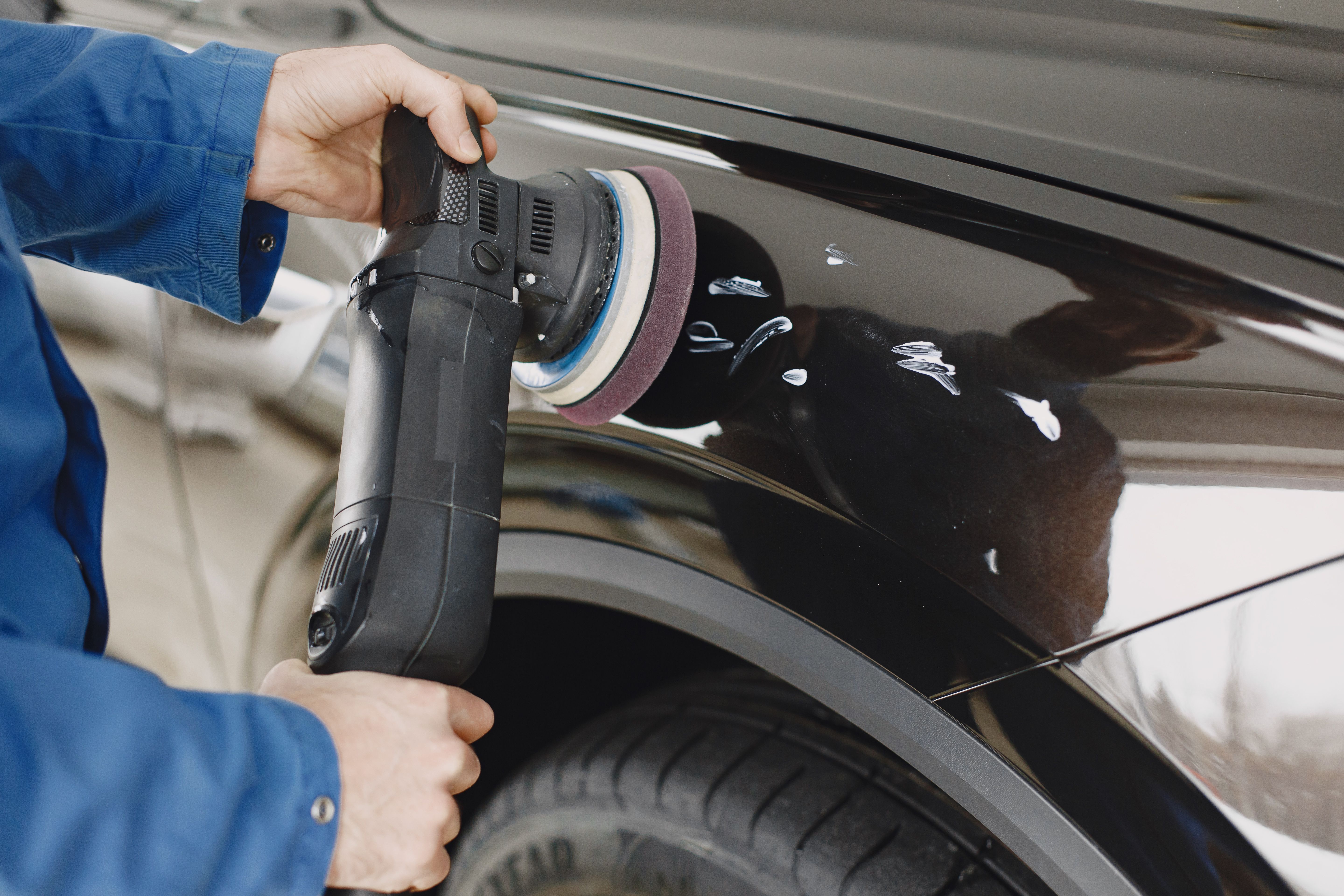 Close-up of hands polishing a vehicle body panel in a workshop.